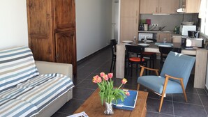 En stue med en sofa, et sofabord med en vase blomster, og et spiseområde med stole og et bord.