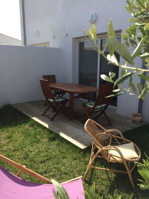 A patio with a wooden table and chairs, a small garden, and a sliding glass door. - Presqu'ile dans l'île, Pretty 3* house, town center, 4 pers, enclosed garden + garage (Loix)