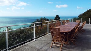 Terraza de madera con mesa y sillas con vista al mar.