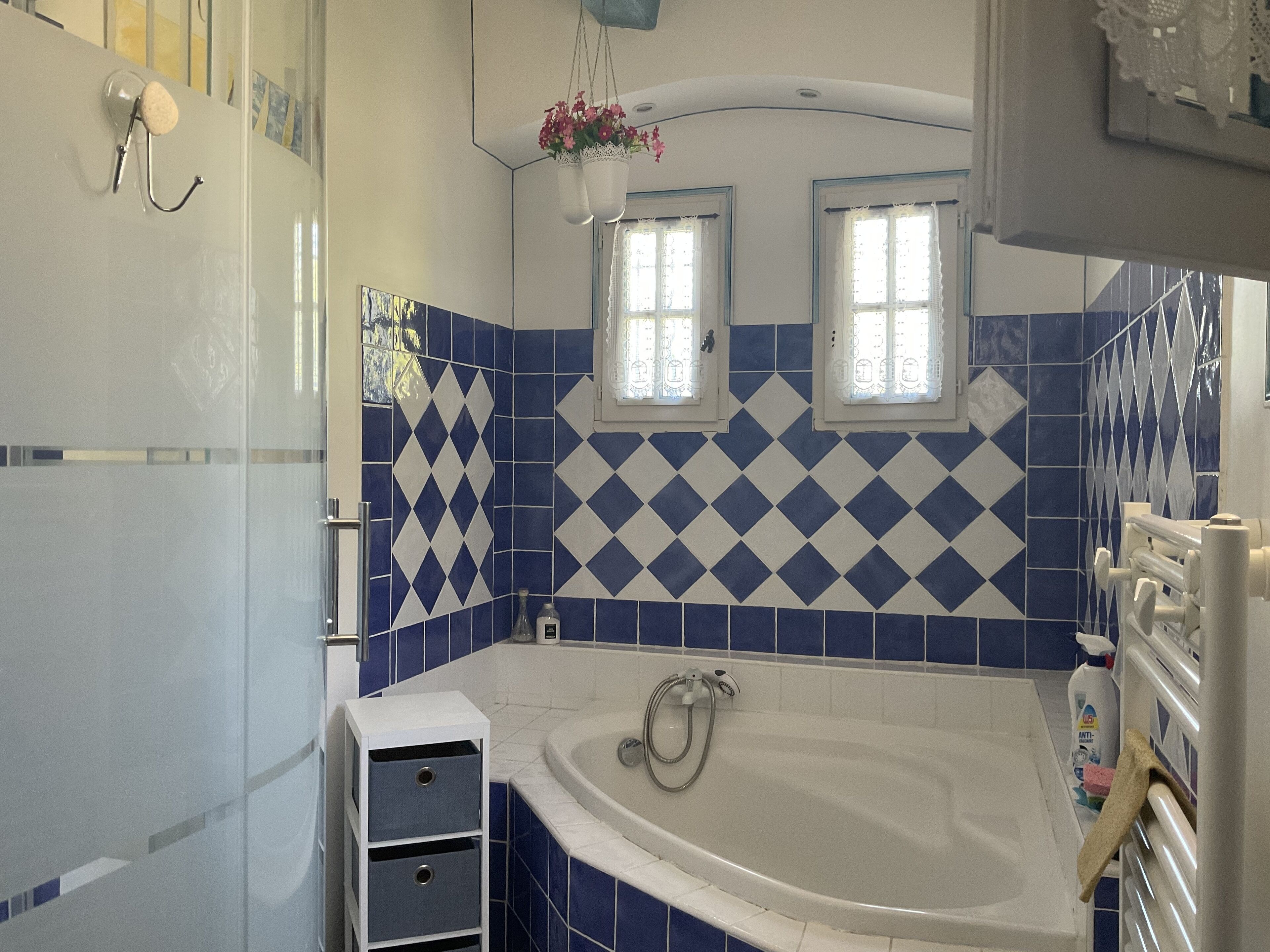Une salle de bain avec une baignoire, deux fenêtres et des carreaux bleus et blancs.