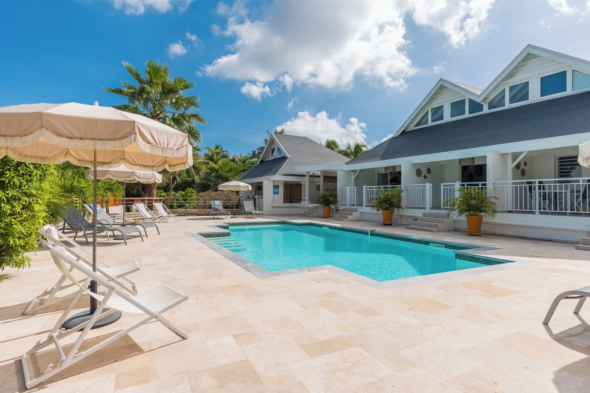A swimming pool with lounge chairs and umbrellas, surrounded by a house with a balcony and potted plants.