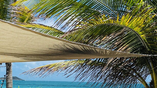 Ein Sitzbereich am Strand mit Tisch, Stühlen und Sonnenschirmen, mit Blick aufs Meer.