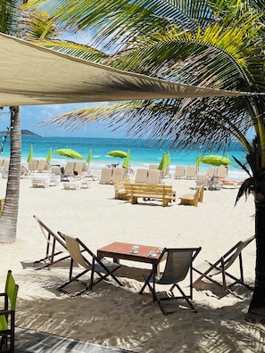 A beachside seating area with a table and chairs, umbrellas, and a view of the ocean.