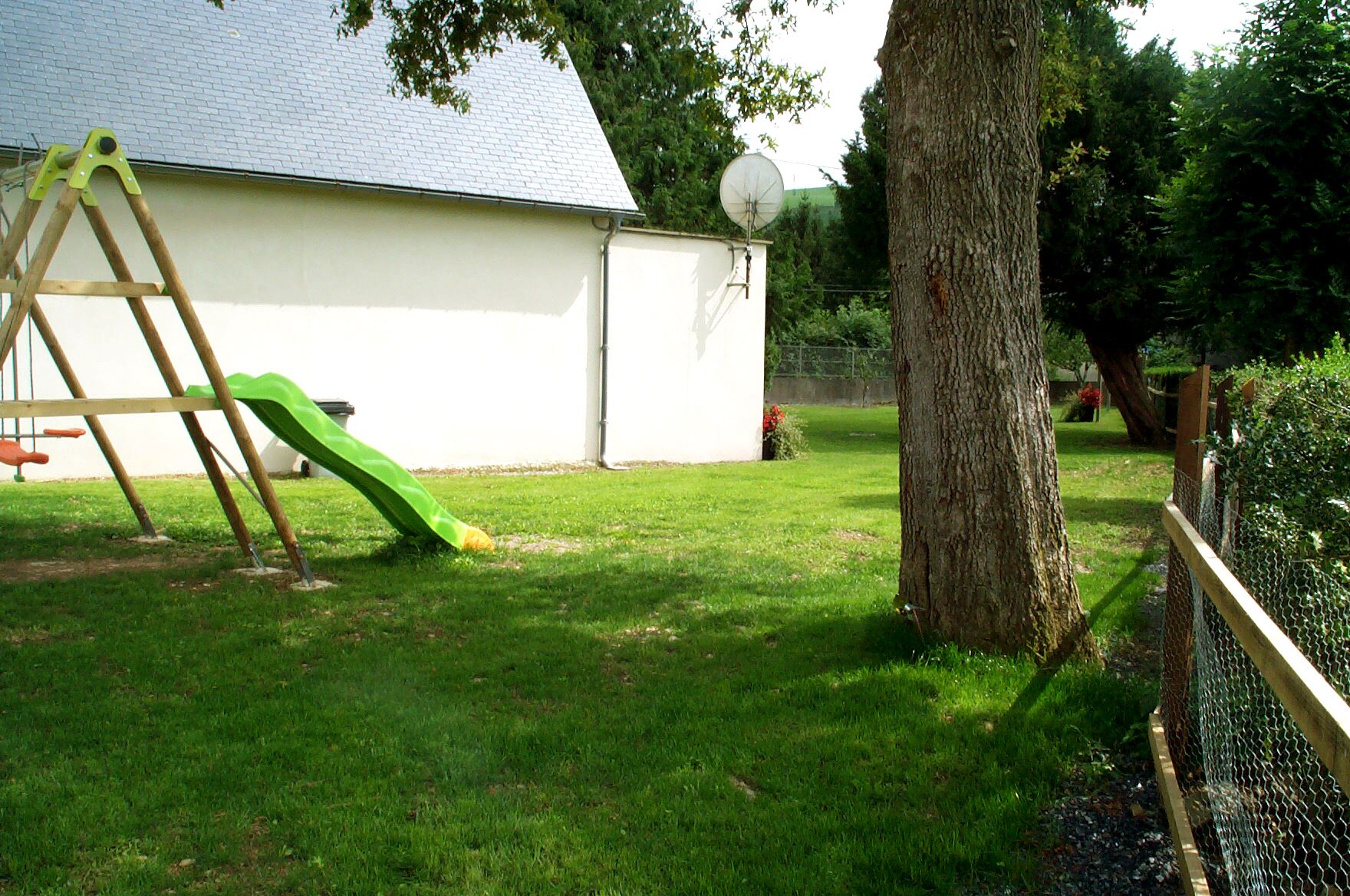 A backyard with a wooden ladder, a green slide, a white building, and a satellite dish.