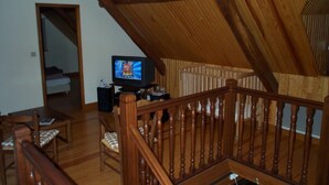 A loft-style room with a wooden staircase, a television, and a bed in the background. - Maison Pyrénées, 3*, south-facing, Mosquito nets, Fibre, Livebox, 2Tv, Enclosed park. (Ossun-Ez-Angles)