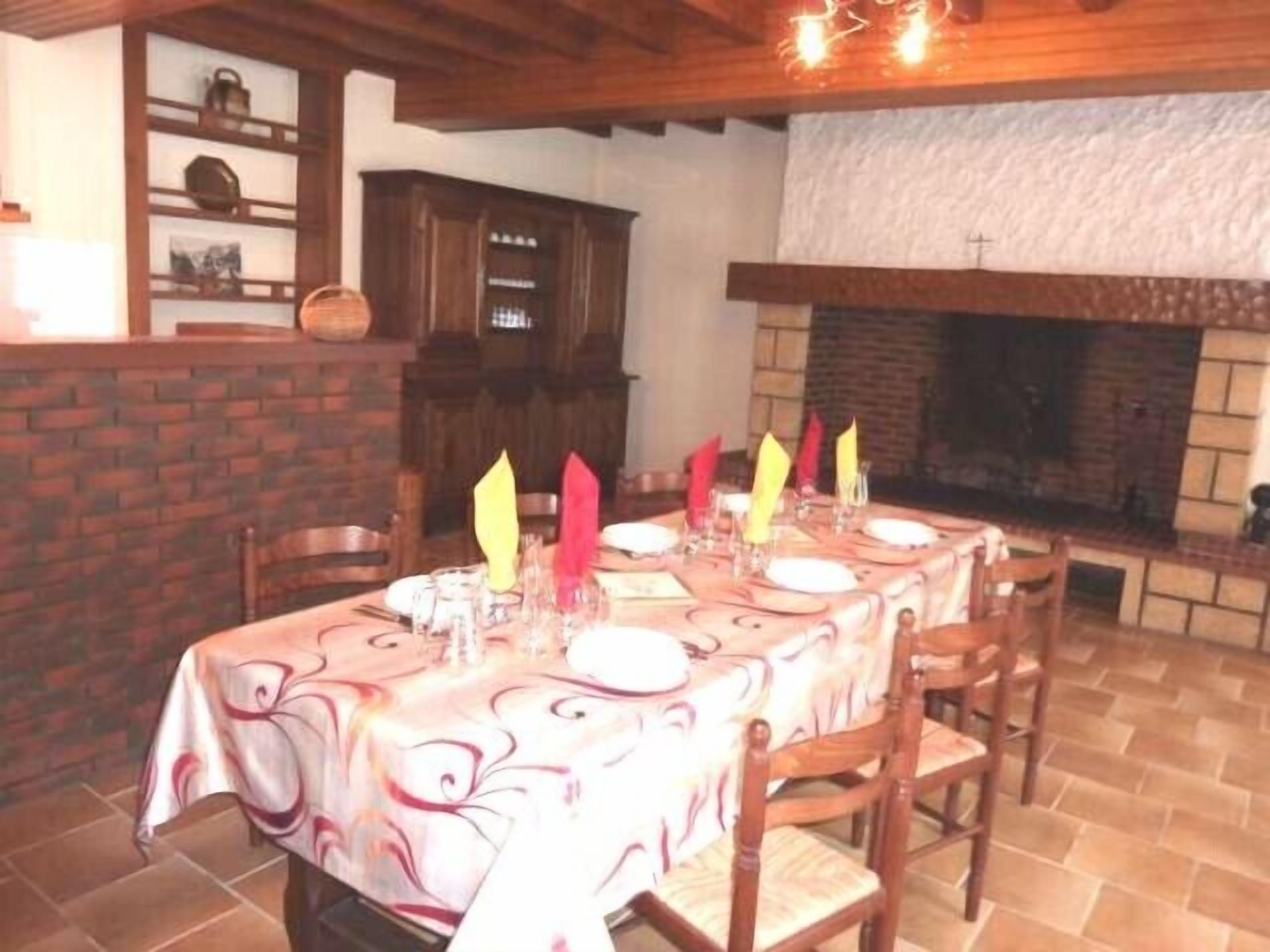 A dining area with a brick fireplace, wooden chairs, and a table set with plates and glasses.