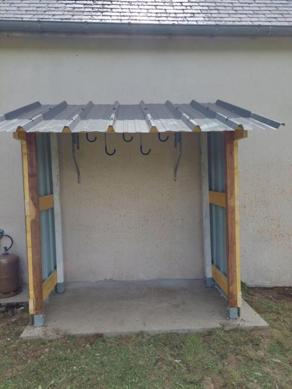 Un petit espace extérieur clos, doté d’un toit en métal et d’un sol en béton, et entouré d’un mur.