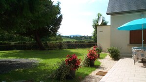 A backyard with a barbecue grill, potted plants, a patio table with an umbrella, and a view of the countryside. - Maison Pyrénées, 3*, south-facing, Mosquito nets, Fibre, Livebox, 2Tv, Enclosed park. (Ossun-Ez-Angles)