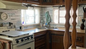 A kitchen with wooden cabinets, a white stove, a window with blinds, and a clock on the wall. - Ocean Lakes Cottage Quiet Street, Shady Lot, 5000 Section Sleeps 7 (Myrtle Beach)