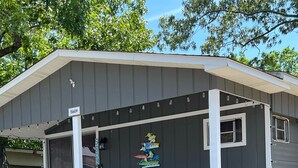 A covered porch with a wooden railing, a small table, and a chair. - Ocean Lakes Cottage Quiet Street, Shady Lot, 5000 Section Sleeps 7 (Myrtle Beach)