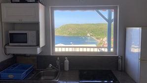 A kitchen with a view of a coastal landscape, a microwave, a sink, and a stove. - Exceptional panoramic view and proximity to the beach (97217 Les Anses d'Arlet)