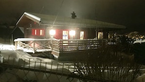 En snedækket bygning med en træterrasse og et hegn i forgrunden.