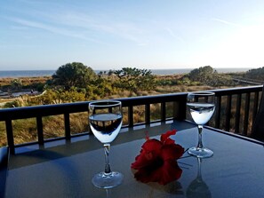 A table with two wine glasses and a red flower on a balcony overlooking a coastal landscape.