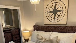 Un letto rifatto con cura, asciugamani arrotolati, una lampada da comodino e un'opera d'arte raffigurante una bussola sulla parete.