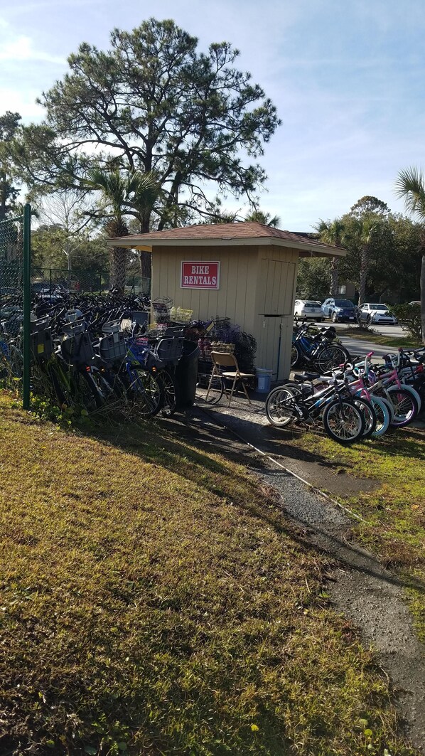 A bike rental station with a sign, bicycles, and a small shed.