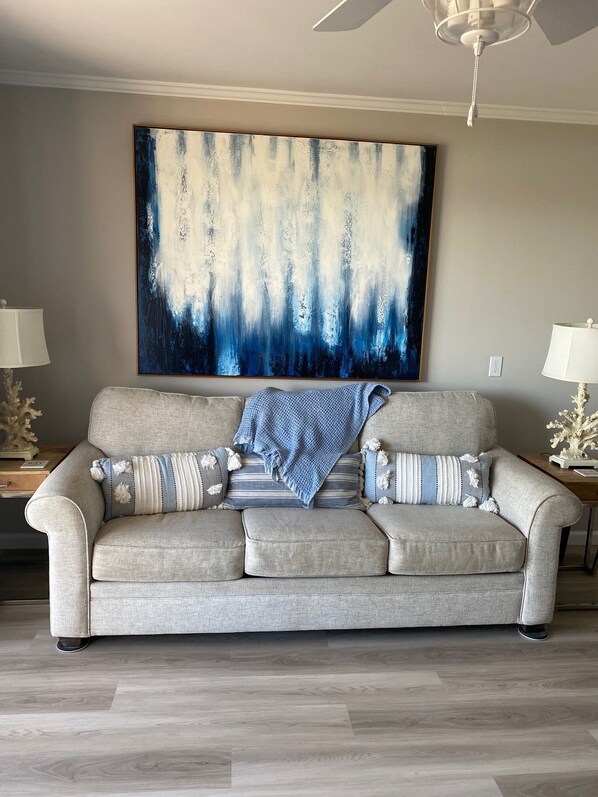 A living room with a beige sofa, a large abstract painting, and two lamps on side tables.