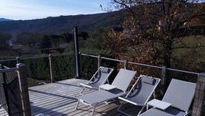 Een houten terras met vier witte loungestoelen en een tafel, omringd door een metalen balustrade.