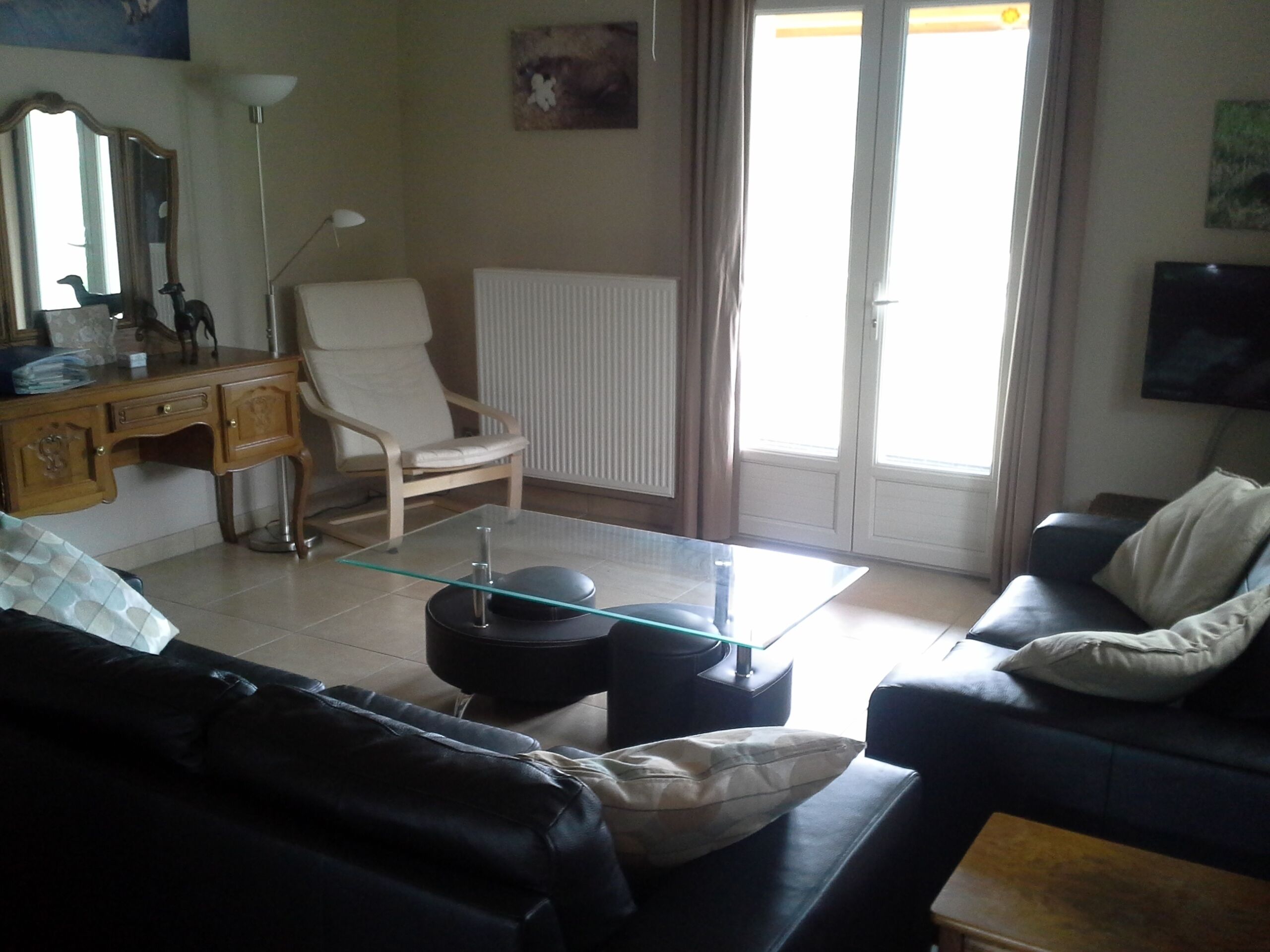 A living room with a glass coffee table, a sofa, a chair, a desk, and a television.