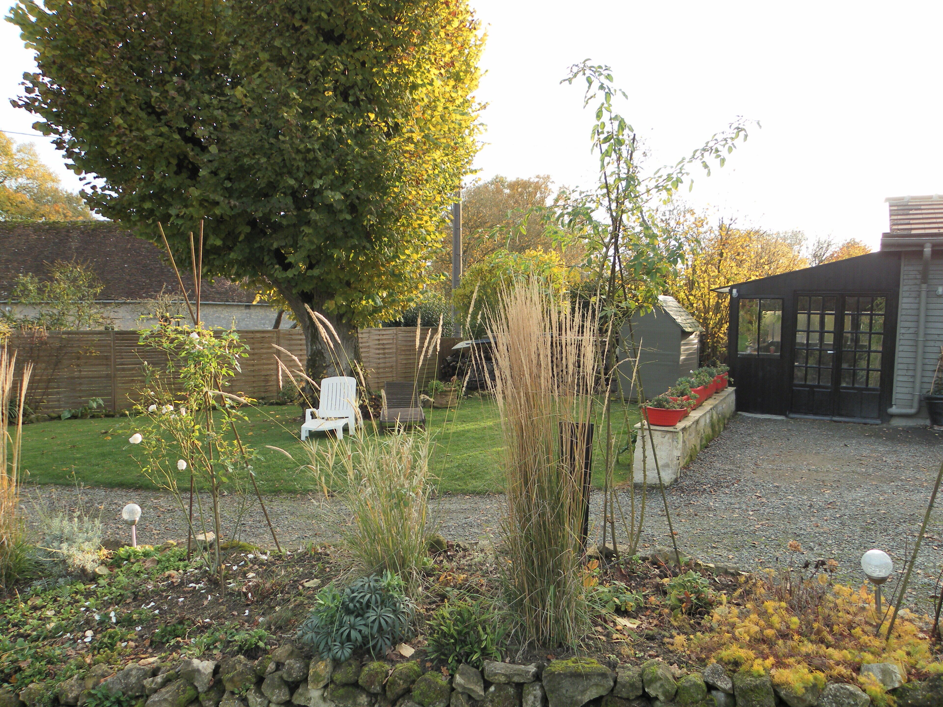 A garden with a white chair, a stone wall, and a shed.