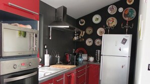 A kitchen with red cabinets, a white refrigerator, a microwave, and an oven. There are plates with designs on the wall. - CHARMING COUNTRY HOUSE WITH WIFI (Perche En Nocé)