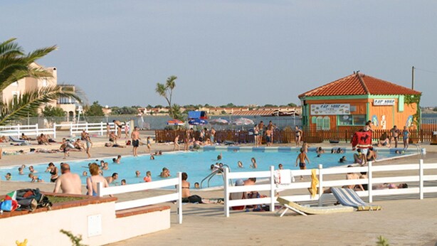 Zona de piscina con un deck cercado, sillas de descanso y una estación de salvavidas.