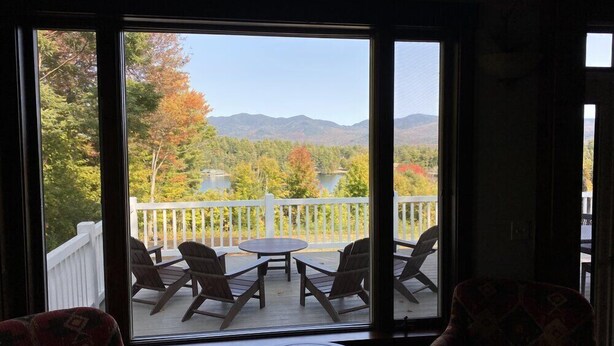 A room with a large window overlooking a deck with outdoor furniture and a scenic view of mountains and trees. - Veranda 4 Bedroom Unit 1 (Lake Placid)