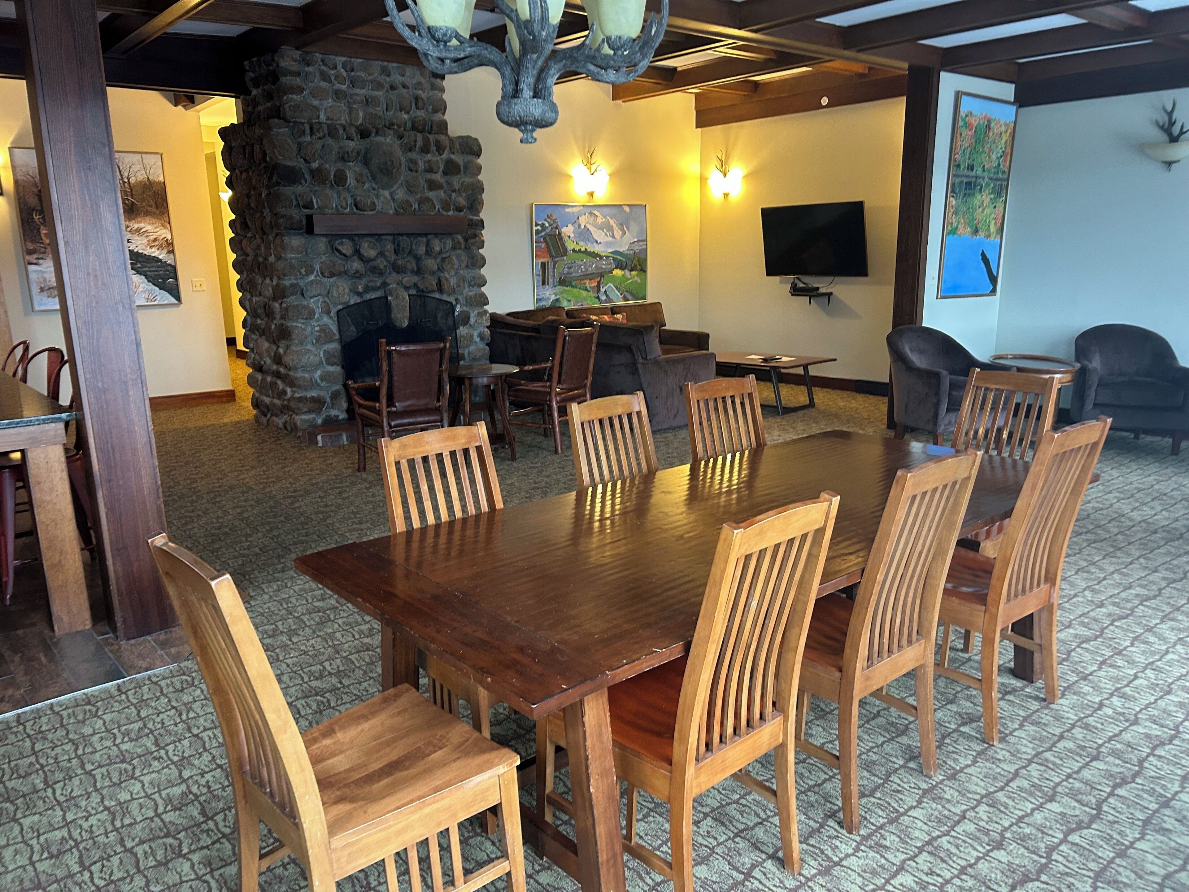 Un coin repas avec une grande table et des chaises en bois, une cheminée en pierre et un téléviseur fixé au mur.