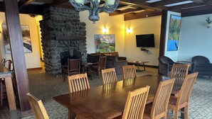 A dining area with a large wooden table and chairs, a stone fireplace, and a television on the wall. - Veranda 4 Bedroom Unit 1 (Lake Placid)