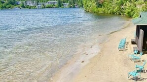 A lakeside view with a sandy beach, lounge chairs, and a forested area. - Veranda 4 Bedroom Unit 1 (Lake Placid)