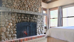 A stone fireplace with a metal screen, a bed with white bedding, and a window with curtains. - Veranda 4 Bedroom Unit 1 (Lake Placid)