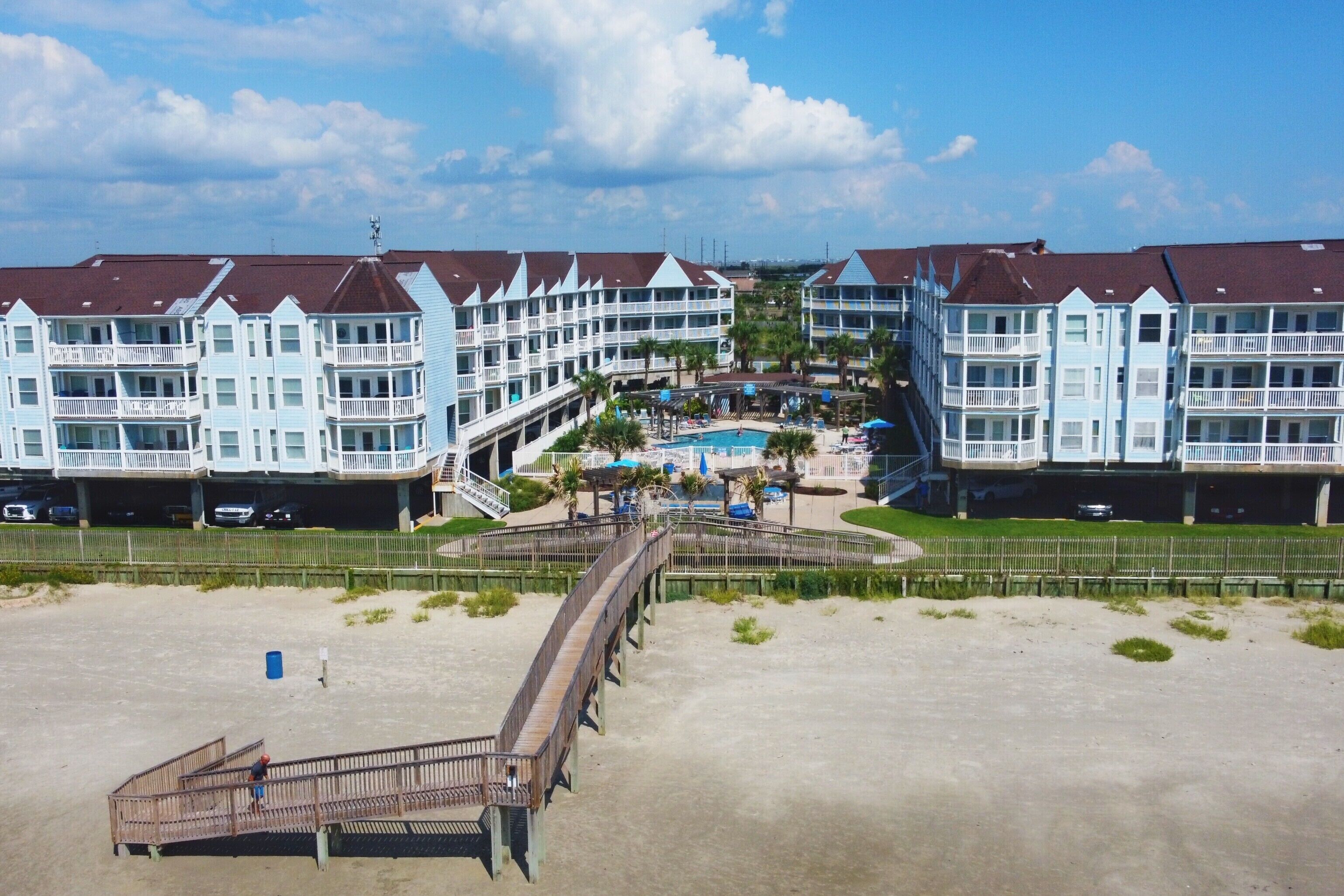 Ein Strandhotel mit mehreren Balkonen, einem Schwimmbad und einer Promenade, die zum Strand führt.