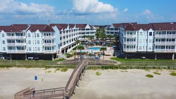 Ein Strandhotel mit mehreren Balkonen, einem Schwimmbad und einer Promenade, die zum Strand führt.