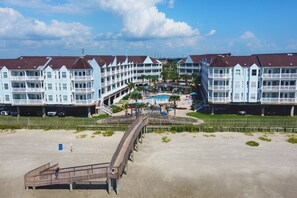 Ein Strandhotel mit mehreren Balkonen, einem Schwimmbad und einer Promenade, die zum Strand führt.