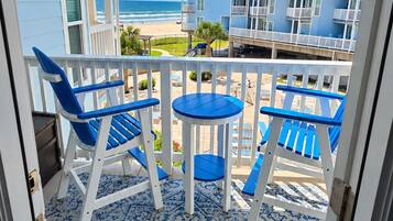 A balcony with blue chairs and a table, overlooking a beach and buildings.