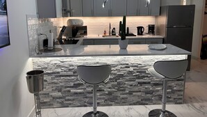 Une cuisine moderne avec des meubles gris, un îlot central doté de tabourets de bar, une cuisinière encastrée et un réfrigérateur.