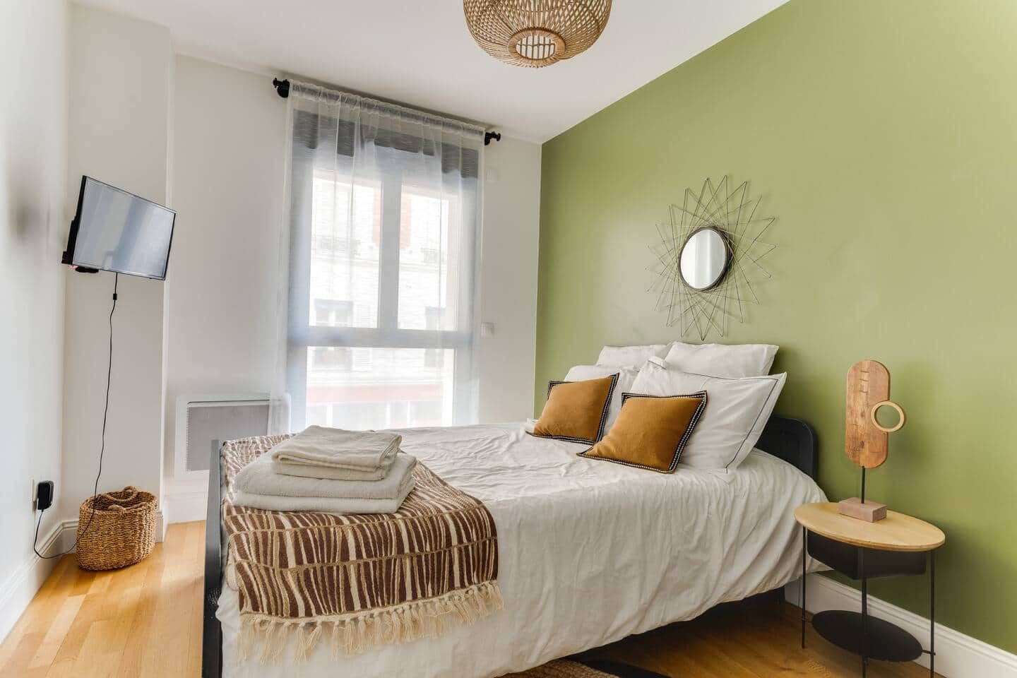 Un dormitorio con cama, televisión, ventana y pared verde.