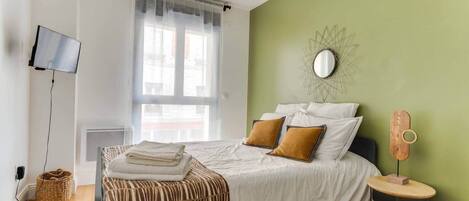 Un dormitorio con cama, televisión, ventana y pared verde.