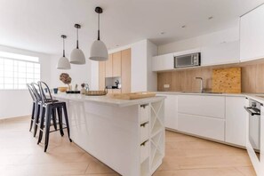 A modern kitchen with white cabinetry, a central island, pendant lighting, and a view of the outdoors. - Palais des Congrès 4 beds adapted for reduced mobility (Levallois-Perret)