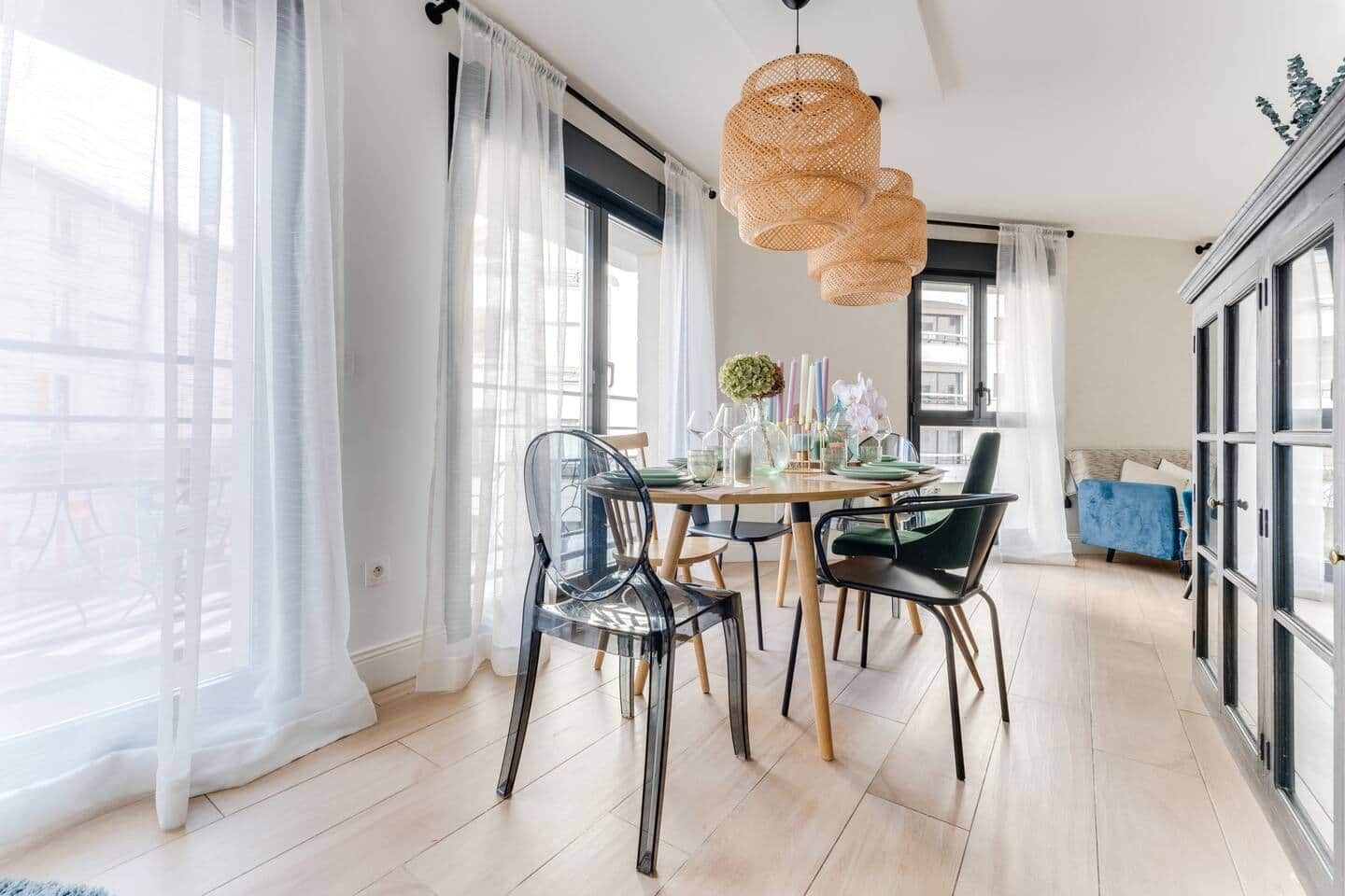 A modern dining area with a table set for four, clear chairs, and a hanging rattan light fixture.