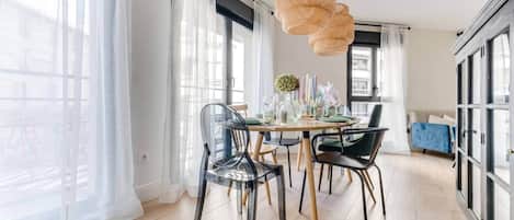 Un comedor moderno con una mesa preparada para cuatro personas, sillas transparentes y un colgante de ratán.