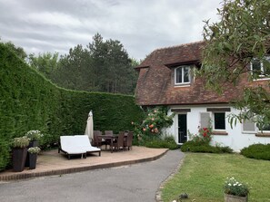 Una casa con un patio empedrado, muebles de exterior y un jardín con diversas plantas y flores.