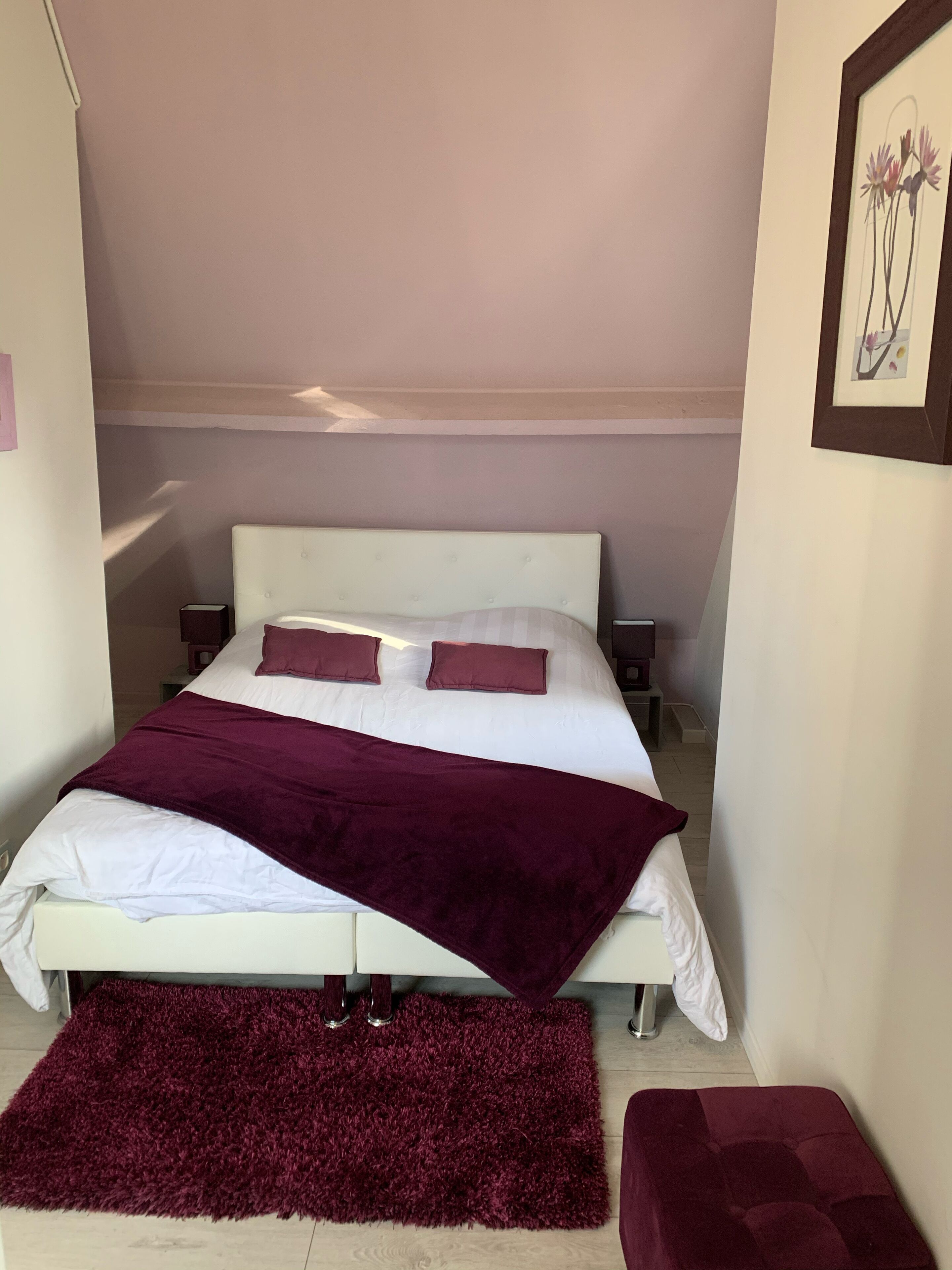 A neatly made bed with a white headboard, two pillows, and a maroon blanket.