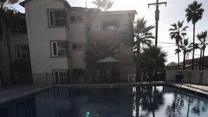 Ein Pool mit gefliesten Rändern, umgeben von einem Gebäude mit vielen Fenstern und einer Palme im Hintergrund.