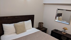 Ein ordentlich bezogenes Bett mit Holz-Kopfteil, ein Nachttisch mit Lampe und ein Spiegel an der Wand.