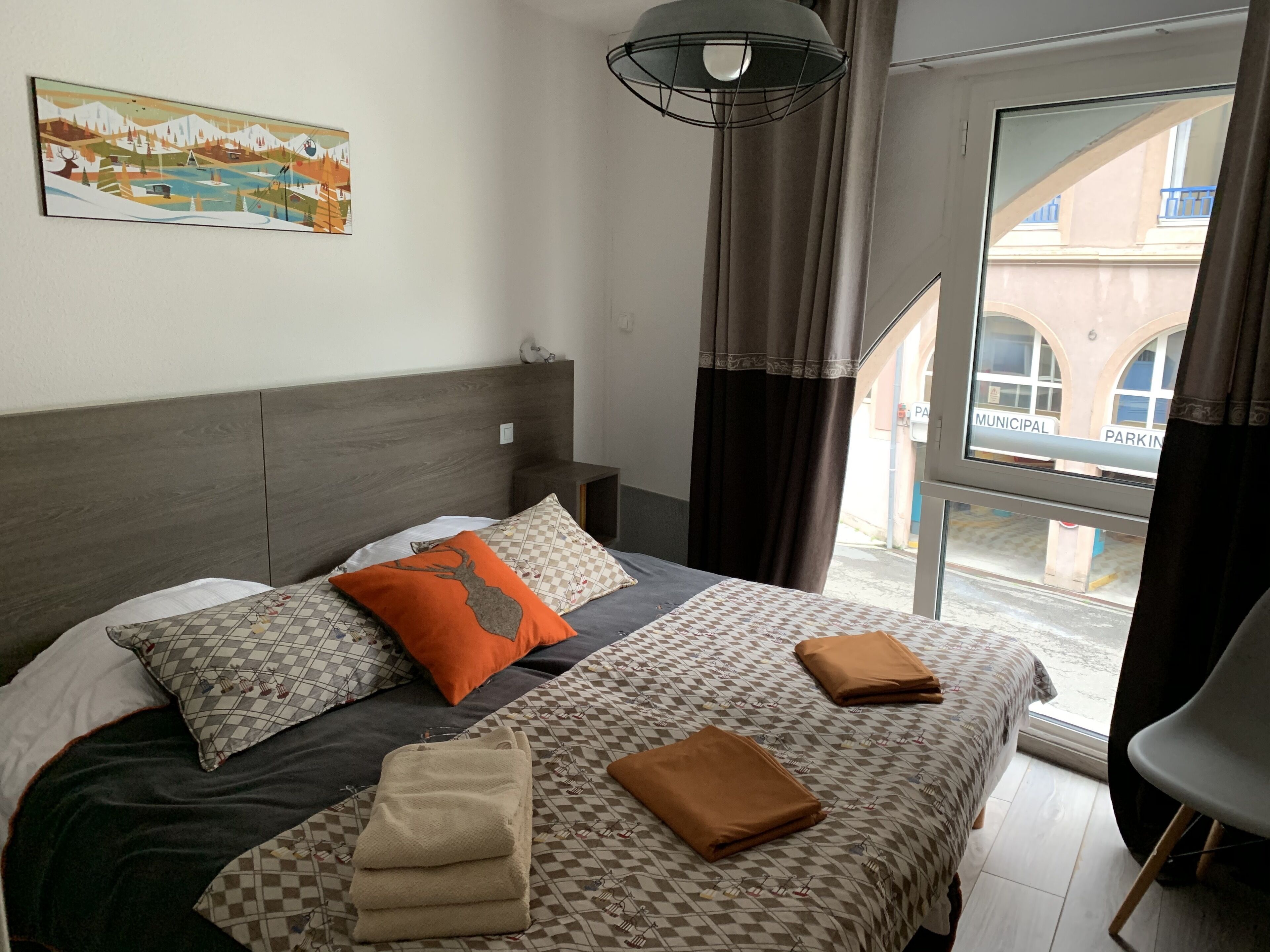 Camera d'albergo con un letto, una finestra con tende e vista su un edificio, oltre a un quadro appeso al muro.