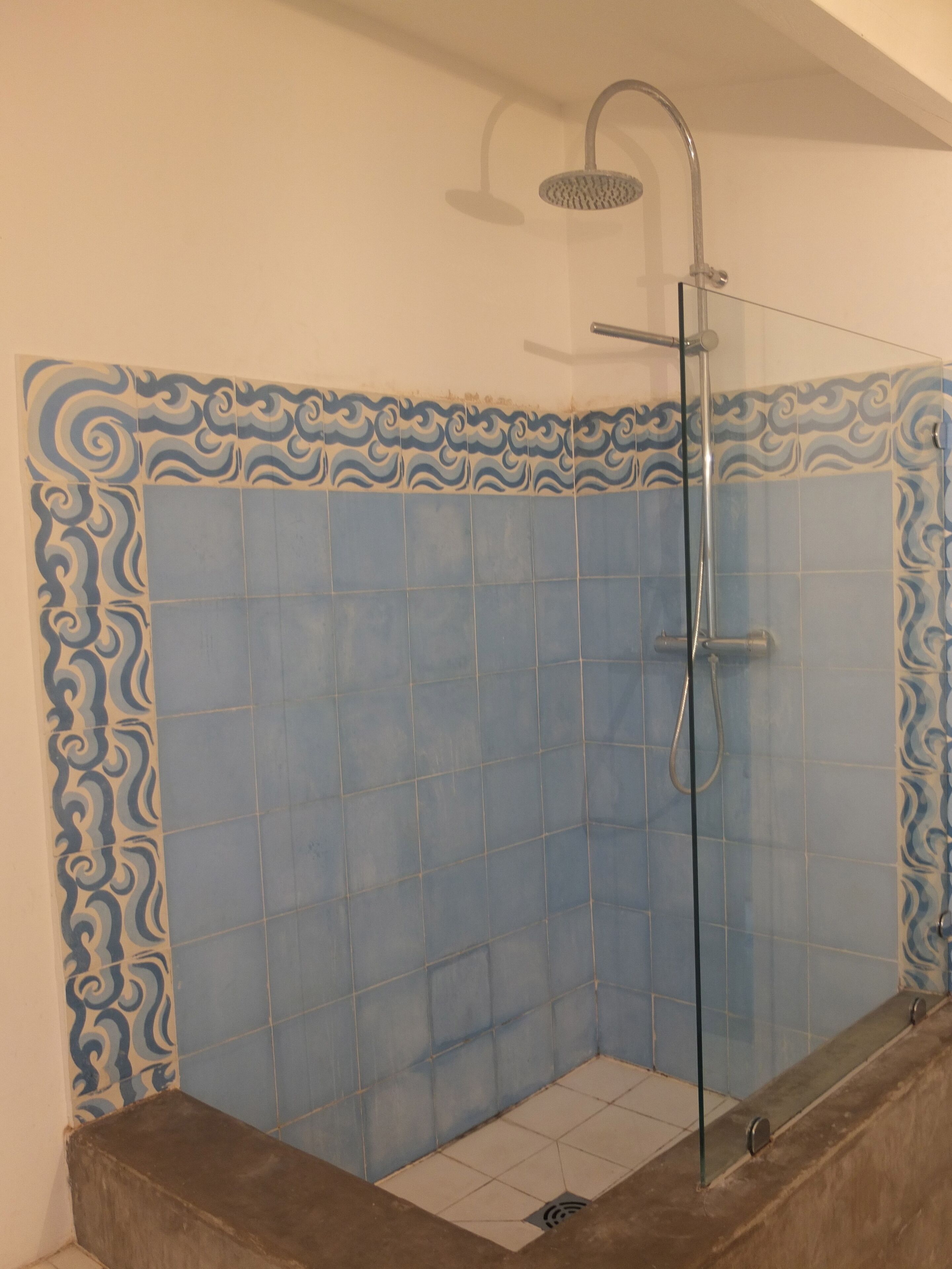 Baño con zona de ducha, azulejos azules y diseños decorativos.