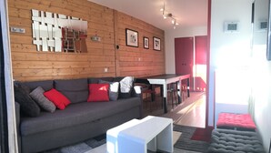 Una sala moderna con un sofá gris, cojines rojos, una mesa de centro blanca y una pared de madera con cuadros enmarcados.
