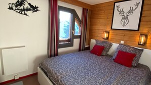 Un dormitorio con cama, ventana, radiador y un cuadro de montañas y ciervos en la pared.
