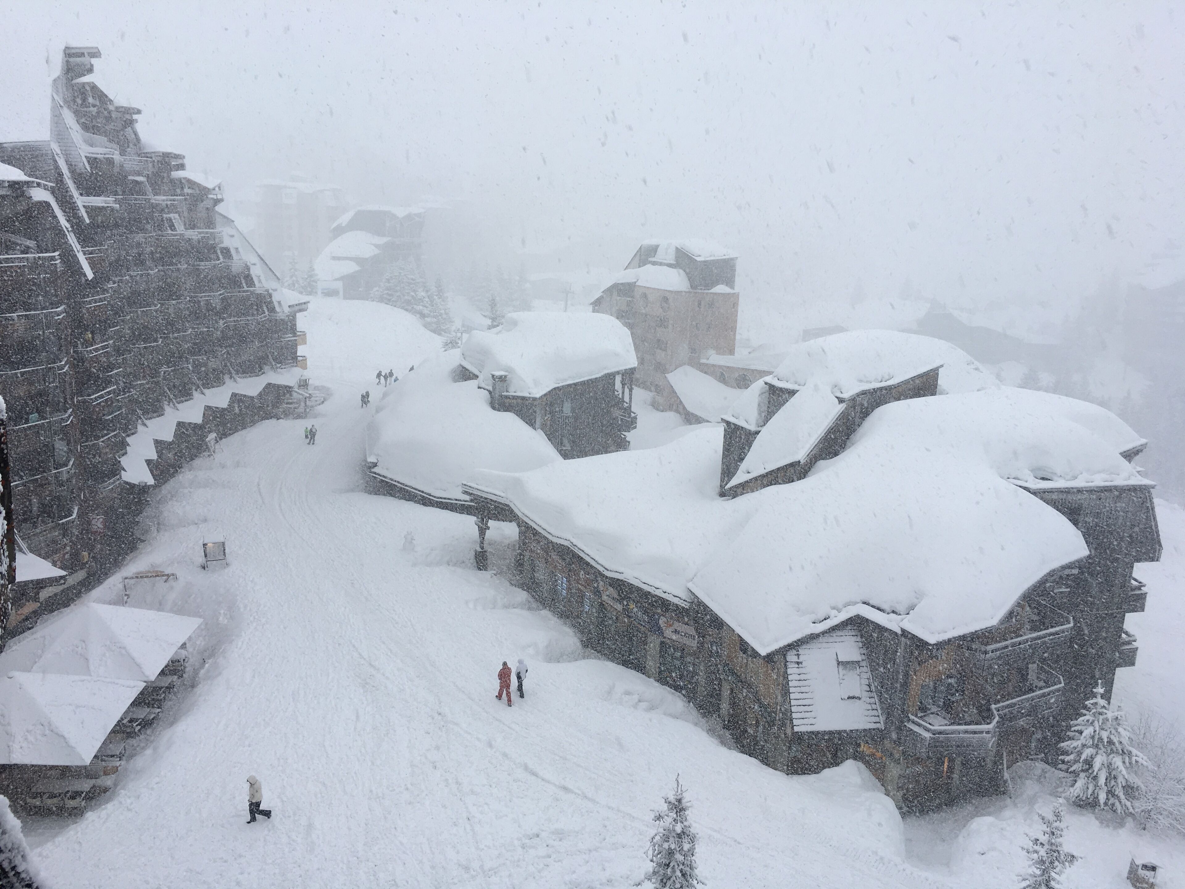 Un complejo invernal cubierto de nieve con varias construcciones tipo chalet, un telesilla y una pista de esquí nevada.