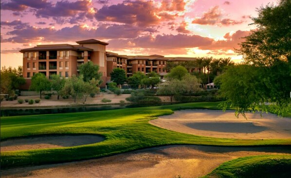 A golf course with bunkers and a large building in the background.